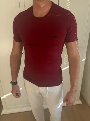 Röd BOSS t-shirt i slim fit - Snygg röd t-shirt från BOSS med diskret logga på bröstet. Modellen är slim fit med korta ärmar och rund halsringning. Perfekt för dig som gillar en stilren och enkel look. T-shirten är gjord i mjuk bomull för maximal komfort.