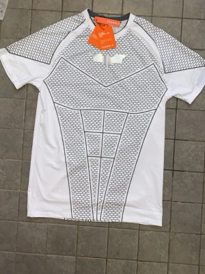 Vit batman compression shirt från youngla  - Vit gymtröja  från youngla compressionshirt batman. Tröjan har korta ärmar, rund hals och är gjord i ett lätt, syntetiskt material som andas. Perfekt för träning och sportaktiviteter.