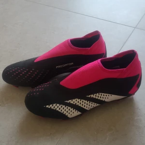 Adidas fotbollsskor - Svarta Adidas Predator fotbollsskor med rosa detaljer, i storlek 43. Använda ett fåtal gånger så fortfarande i mycket bra skick. Nypris 799kr