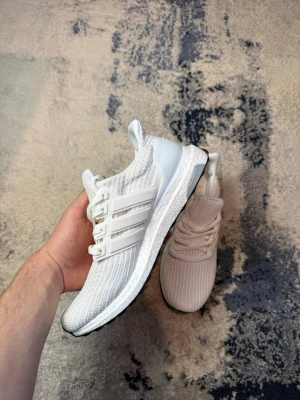 Vita Adidas Ultraboost sneakers - Säljer ett par fräscha vita Adidas Ultraboost sneakers med stickad ovandel, klassiska tre ränder på sidan och svart sula. Skorna har en sportig look med bekväm Boost-mellansula och snörning framtill. Perfekta för dig som gillar stilrena och bekväma sneakers. OBS! Ingen box ingår 