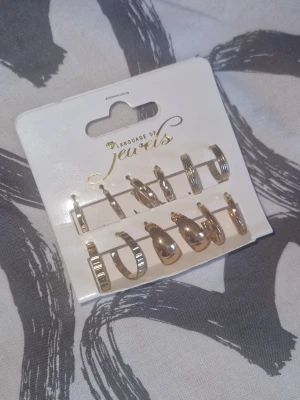 Örhängen - Säljer ett set med sex par guldiga örhängen från Language of Jewels. Olika former och mönster, både släta och räfflade hoops. Perfekta för att mixa och matcha till olika looks. Materialet är metall med guldfinish. Köpt i Grekland