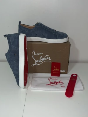 Blåa Christian Louboutin sneakers - Snygga blåa sneakers från Christian Louboutin i mocka med klassisk röd sula och vita kanter. Skorna har lågt skaft, rund tå och matchande blå skosnören. Perfekta för dig som vill sticka ut med exklusiv design och lyxiga detaljer.