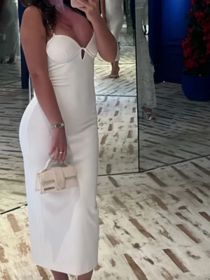 Vit långklänning med hjärtformad byst - Elegant vit långklänning med hjärtformad byst och smala axelband. Klänningen har en figurnära passform och en liten cut-out detalj framtill. Perfekt för dig som vill ha en stilren och modern look.