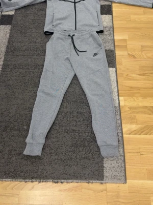 Grå Nike tracksuit  med dragkedja ganska ny limited edition släpptes en gång. - Snygga grå tracksuit  från Nike med svart logga på låret och brösten justerbar dragsko i midjan. Byxorna har ribbade muddar vid bensluten och praktiska fickor, varav en med dragkedja. Perfekta för chill eller träning passa S även xs och m 