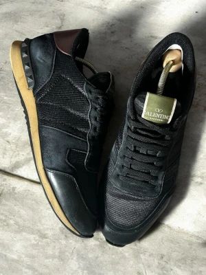 Valentino rockrunners  - Valentino Garavani Rockrunner Sneakers – Svart / Strl42 men passar 42,5 Säljer ett par äkta Valentino Garavani Rockrunner-sneakers i svart. Skorna är i mycket fint skick. – perfekt både för användning och som samlarobjekt.  Skick: ✔ Mycket bra skick  Detaljer: 	•	Modell: Valentino Garavani Rockrunner 	•	Färg: Svart med mörkbruna detaljer 	•	Materialmix med läder, mocka och mesh 	•	Klassiska pyramidnitar vid hälen. Skick- se bilder, sulan lite spräckt längst fram på höger skon