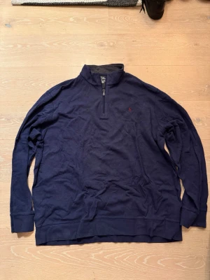 Marinblå tröja från Polo Ralph Lauren - Snygg marinblå långärmad tröja från Polo Ralph Lauren med halv dragkedja och liten röd logga på bröstet. Tröjan har ribbade muddar och är tillverkad i mjukt material som känns skönt mot huden.