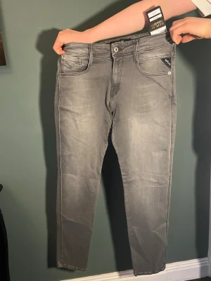 Grå slim fit jeans från Replay - Snygga grå slim fit jeans från Replay med stretch. Klassisk femficksmodell, diskreta slitningar och logga på bakfickan. Perfekta för dig som gillar en modern och stilren look. Nypris 1000 kr