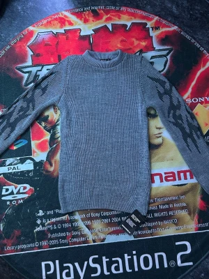 Grå stickad tröja med mönstrade ärmar - Säljer en grå stickad tröja från Reserved med ribbad struktur och coola mörkgrå mönster på ärmarna. Tröjan har rund halsringning och långa ärmar. Perfekt för dig som gillar en stilren men ändå unik look.