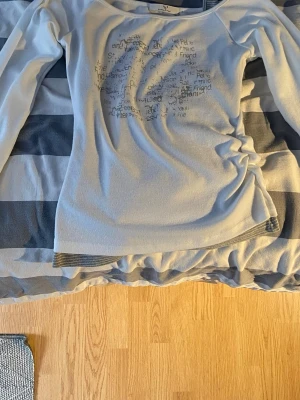 Vit långärmad topp - Säljer en vit långärmad topp  med tryckt textmönster framtill. Toppen har ett grått linne under som är sytt ihop med själva tröjan.