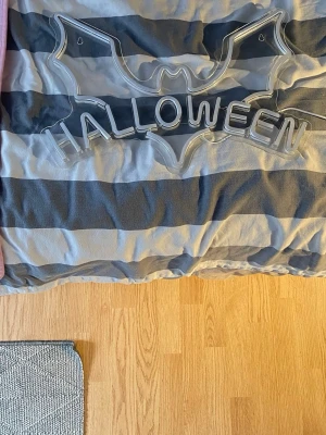Halloween LED-skylt med USB - Cool LED-skylt i genomskinlig plast formad som en fladdermus med texten HALLOWEEN. Kopplas in med vit USB-kabel, perfekt för att skapa halloweenstämning i rummet. Skylten är lätt och enkel att hänga upp tack vare hål i hörnen.