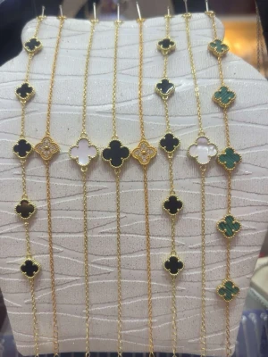 Guldarmband med fyrklöverhängen - Snygga armband i guldton med fyrklöverformade hängen i svart, vitt och grönt. Kedjan är tunn och elegant, och varje hänge har en pärlad kant som ger extra detalj. Perfekt accessoar för att lyfta din stil.