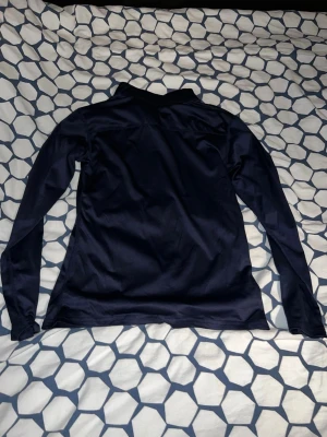 Mörkblå långärmad träningströja - Snygg mörkblå långärmad träningströja med halv dragkedja framtill och hög krage. Tillverkad i ett stretchigt och lätt material som passar perfekt för löpning eller gym. Enkel och stilren design utan synligt märke.