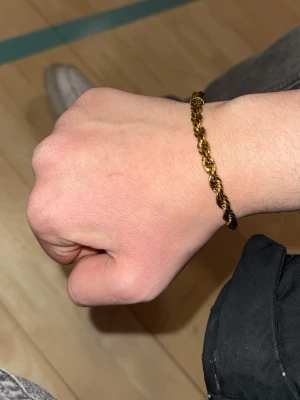 Cordell armband - Snyggt armband i guldfärgad metall med tvinnad design som ger en cool och trendig look. Perfekt accessoar för att lyfta din outfit och passar till många olika stilar. Lätt att bära och matcha med andra smycken.