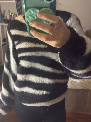 Zebramönstrad stickad tröja Ivyrevel - Säljer en fluffig stickad tröja från Ivyrevel med zebramönster i svart och vitt. Tröjan har en avslappnad passform, långa ärmar och mjukt material som känns riktigt cozy. Perfekt för dig som vill sticka ut med ett djurinspirerat plagg.