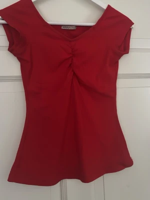 Röd ribbad topp från Anna Field - Snygg röd topp från Anna Field med ribbad struktur och v-ringning. Toppen har korta ärmar och en smickrande rynkning framtill. Perfekt att styla med jeans eller kjol för en trendig look.