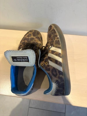 Adidas sneakers med leopardmönster ! 🐆🐆 - Unika Adidas sneakers med leopardmönster och klassiska vita ränder på sidan. Skorna har blå detaljer på insidan och guldiga öljettar. Materialet är textil med gummisula. Perfekt för dig som vill sticka ut med ett djärvt mönster. 