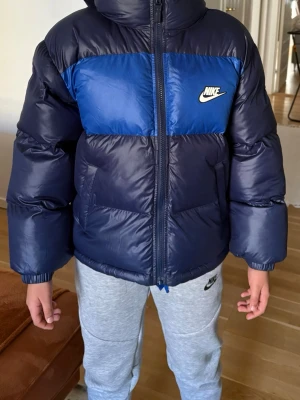 Mörkblå Nike pufferjacka med huva - Säljer denna jacka som min lillebror fick som julklapp. Han tycker inte om den och har aldrig använt den! Helt ny, storlek M(137-147) passar honom som är 149! 