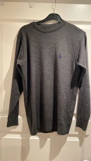 Mörkgrå stickad tröja från Polo Ralph Lauren - Mörkgrå stickad tröja från Polo Ralph Lauren med klassisk blå logga broderad på bröstet. Tröjan har rund halsringning och långa ärmar. Perfekt för lager på lager och enkel att matcha till olika outfits. Pris går att diskutera 