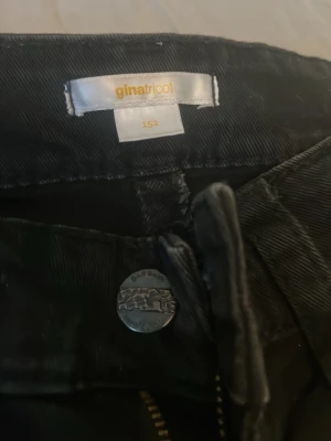 Svarta jeans från Gina Tricot - Säljer ett par svarta jeans från Gina Tricot i storlek 152. Jeansen har en snygg ficka med knappdetalj bak och klassisk dragkedja framtill. Perfekta till en cool och avslappnad stil.