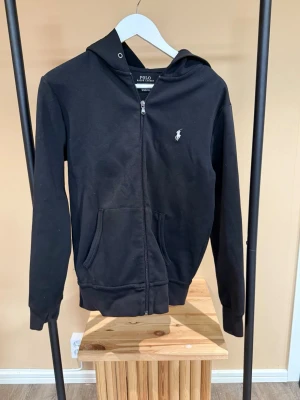 Poloralphlauern Hoddie  - Säljer en svart fin polo Ralph lauern hoddie med vita detaljer med dragkedja och luva.