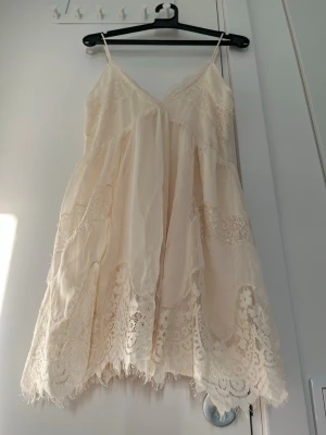 Ljus spetsklänning med tunna band, XS - Söt ljus kortklänning med tunna axelband och v-ringning. Klänningen har fina spetsdetaljer och volangkant nedtill, vilket ger en romantisk känsla. Perfekt för varma dagar och sommarens alla tillfällen. XS, ny med label. 