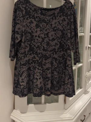 Blommig topp från XLNT, svart/grå - Snygg topp från XLNT i svart och grått med blommigt mönster. Toppen har trekvartsärm och rund halsringning.
