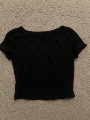 Svart croppad topp med kort ärm - En enkel svart croppad topp med rund halsringning och korta ärmar. Perfekt att matcha med höga jeans eller kjol för en clean och stilren look. Tunn och mjuk i materialet. 
