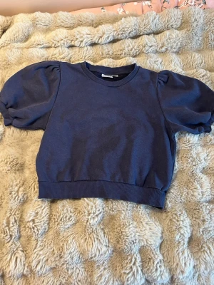 Mörkblå topp med puffärmar  - Trendig mörkblå topp med puffiga korta ärmar och ribbad kant nedtill. Perfekt för dig som gillar en enkel men ändå snygg look. 