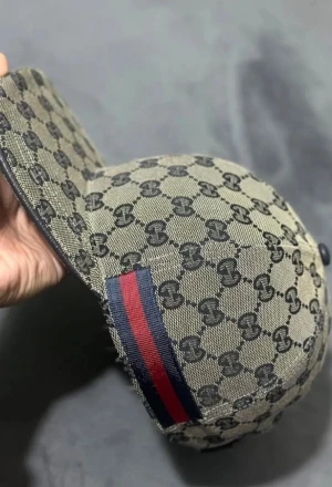 Gucci beige keps med GG-mönster - Säljer en beige keps från Gucci med det klassiska GG-monogrammönstret över hela kepsen. På sidan finns en ikonisk röd och marinblå rand. Kepsen har justerbar rem bak och är tillverkad i canvasmaterial.