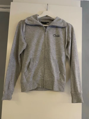 Grå zip hoodie från Oxide - Snygg gråmelerad hoodie från Oxide med dragkedja framtill och två fickor. Klassisk huva och ribbade muddar vid ärmslut och nederkant. Perfekt för en avslappnad och sportig stil. Materialet känns mjukt och bekvämt mot huden, jötte skön älskar. Ej bra pris,,skriv till mig (kan användas som storlek S men lite tajtare)