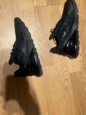 Nike Air Max 270 helsvarta sneakers - Snygga helsvarta Nike Air Max 270 sneakers med mesh-ovandel och stor synlig Air-enhet i hälen. Skorna har en sportig siluett, diskret Swoosh-logga och bekväm passform. Perfekta för dig som gillar stilrena och moderna sneakers.