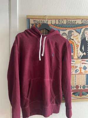 Vinröd hoodie från Polo Ralph Lauren - Snygg vinröd hoodie från Polo Ralph Lauren med klassisk huva och vita dragsnören. Har en liten broderad logga på bröstet och tillverkad i mjukt bomullsmaterial som är perfekt för chill dagar.                                                      Byten kan vara intressant!