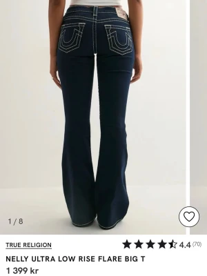 True Religion mörkblå flare jeans - Snygga mörkblå jeans från True Religion med låg midja och utsvängda ben. Tydliga kontrastsömmar och ikoniska bakfickor med broderad logga. Storlek W25 vilket motsvarar ungefär S. Aldrig använda, bara testade.