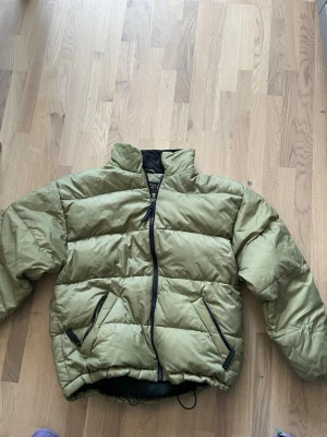 Olivgrön pufferjacka från Conquest - Säljer en olivgrön pufferjacka från Conquest med svarta detaljer och dragkedjor. Jackan har hög krage, två snedställda fickor med dragkedja och svart innerfoder. Perfekt för kalla vinterdagar och riktigt skön att bära.     Stor i storlek 