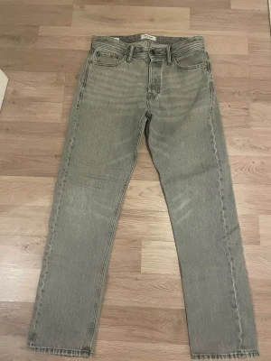 Grå raka jeans från Jack&jones  - Säljer ett par grå raka jeans från jack%jones med klassisk femficksmodell och normal midja. Jeansen har en snygg tvättad look och är tillverkade i denim av bomull. Perfekta för en avslappnad och stilren outfit. Storlek W29 L32 köpta från jack&jones för runt 800 spänn.
