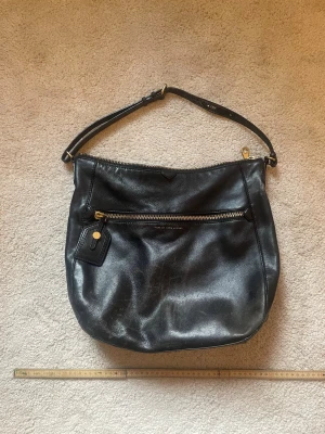 Svart läderväska Marc by Marc Jacobs - Snygg svart handväska i mjukt läder från Marc by Marc Jacobs. Väskan har en justerbar axelrem, guldfärgade detaljer och en stor dragkedjeficka framtill. Klassisk och rymlig modell med diskret logga på framsidan. Mammas gamla väska den är 100 äkta 