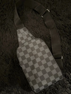 Louis Vuitton axelväska  - Snygg axelväska från Louis Vuitton i klassiskt svart och grått damier-mönster. Väskan har justerbar bred axelrem och dragkedja. Priset kan diskuteras vid snabb affär.