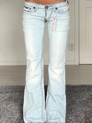 Ljusblå raka jeans från Miss Sixty - Säljer ett par ljusblå jeans från Miss Sixty med raka ben och klassisk femficksmodell. Jeansen har en snygg tvättad look, röda detaljer på knappen och insidan av linningen samt kontrastsömmar. Perfekta för en avslappnad och trendig stil.