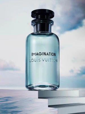 Louis Vuitton Imagination parfym - Lyxig parfym från Louis Vuitton i en elegant, rund glasflaska med ljusblått innehåll och svart lock. Flaskan har stilren text med 'IMAGINATION' och 'LOUIS VUITTON' ingraverat. Kommer i en vit, cylinderformad förpackning med matchande design. 100ml