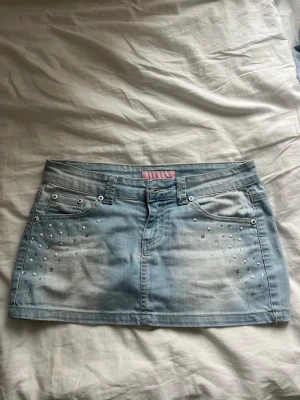 Ljusblå jeanskjol - Snygg kort ljusblå jeanskjol men rosa detaljer och nitar/glitter. Står att det är storlek L men den passar mig som har S. Märket är miss sexy men köpt vintage i Italien.