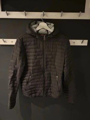 Svart pufferjacka från Colmar - Säljer en svart pufferjacka från Colmar med huva och dragkedja framtill. Jackan har två sidofickor med dragkedja och ett Colmar-märke på ena ärmen. Lätt vadderad och perfekt för kalla dagar. Klassisk quiltad design och sportig look.