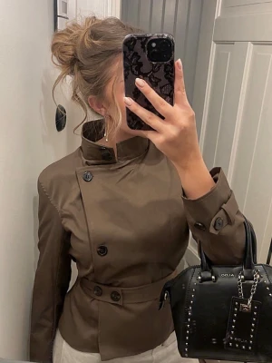 Trenchcoat  - Verkligen en drömmig chic vårkappa / trenchcoat med knytning i midjan (knäppning?). Kappan är kort och brun i strl XS, samt kan knäppas hela vägen upp i kragen eller användas som en skepparkappa beroende på vad man föredrar. Helt oanvänd men säljer då den var lite liten på mig😽💕💕