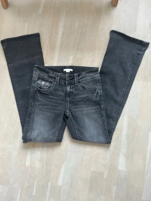 Grå bootcut jeans med slitningar - Säljer ett par grå bootcut jeans med snygga slitningar och kontrastsömmar. Jeansen har låg midja, fem fickor och dubbla knappar i linningen. Perfekta för en avslappnad och trendig look.