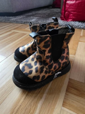 Leopardmönstrade boots med dragkedja - Snygga boots med leopardmönster och svarta detaljer. Bootsens ovandel är i konstläder med svart tåparti och elastiska paneler på sidorna. Dragkedja på insidan för enkel på- och avtagning. Perfekta för dig som vill sticka ut med din stil.