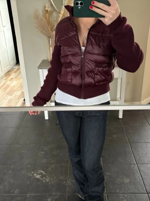 Vinröd cardiganjacka med dragkedja - Snygg vinröd cardiganjacka med quiltad framsida och stickade ärmar samt muddar. Jackan har dragkedja framtill, två stora fickor och ribbad krage. Perfekt för dig som vill ha en trendig och mysig look. Från Gina Young i storlek L men sitter perfekt på S/Xs.  