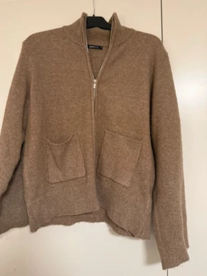 Beige ziptröja med fickor Gina Tricot - Mysig beige ziptröja från Gina Tricot med två stora framfickor och hög krage. Tröjan är stickad i ett mjukt material och har ribbade muddar vid ärmslut och nederkant. Perfekt för lager på lager och enkel att matcha.