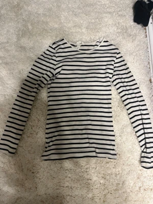 Randig långärmad topp H&M - Klassisk långärmad topp från H&M med svarta och vita horisontella ränder. Tunn och mjuk i bomullsmaterial, perfekt för lager på lager eller som den är. Enkel och tidlös design med rund halsringning.