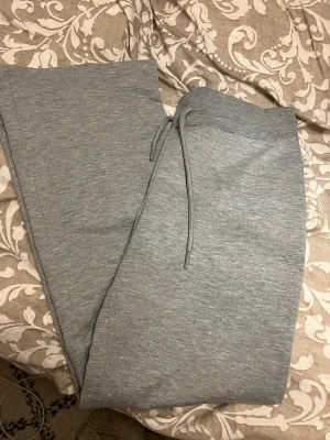 Grå mjukisbyxor - Säljer ett par klassiska grå mjukisbyxor med raka ben och dragsko i midjan. Byxorna är tillverkade i mjukt och stretchigt material, perfekta för chill dagar. Inga synliga loggor eller märken. Passar dig som gillar enkel och clean stil.