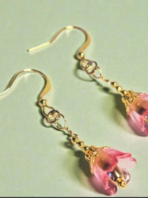 Rosa blomformade örhängen med pärlor - Unika örhängen i form av rosa blommor med guldfärgade detaljer och små pärlor inuti. Hängande modell med krok av guldpläterat stål, tillverkade i metall och akryl. Perfekta för dig som vill ha en söt och romantisk look.