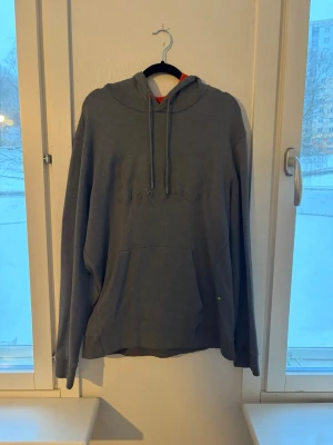 Grå hoodie från Hugo Boss - Snygg grå hoodie från Hugo Boss med diskret broderad logga på bröstet. Hoodien har huva med dragsko och en stor magficka framtill. Tillverkad i mjukt material som känns skönt mot huden. Perfekt för en avslappnad och stilren look.
